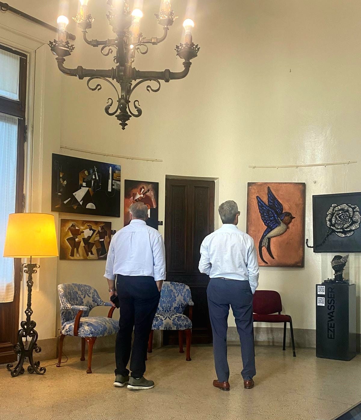 Salón del palacio con visitantes recorriendo obras bajo una araña de cristal