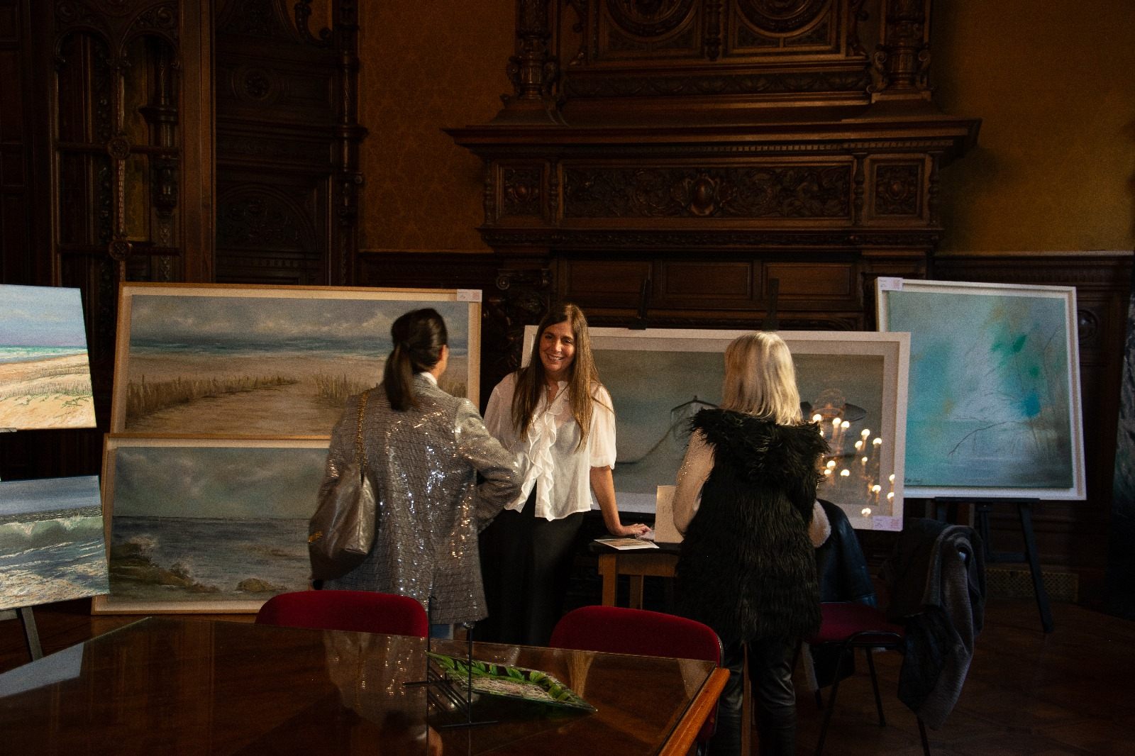 Artista conversando con visitantes junto a sus obras de paisajes marinos